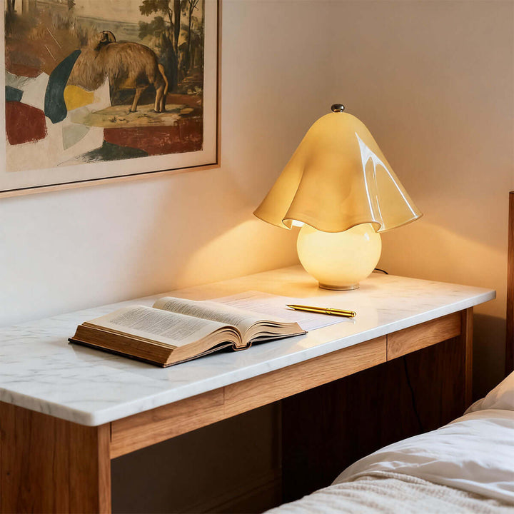 Frosted amber flower table lamp beside an open book on a marble bedroom desk