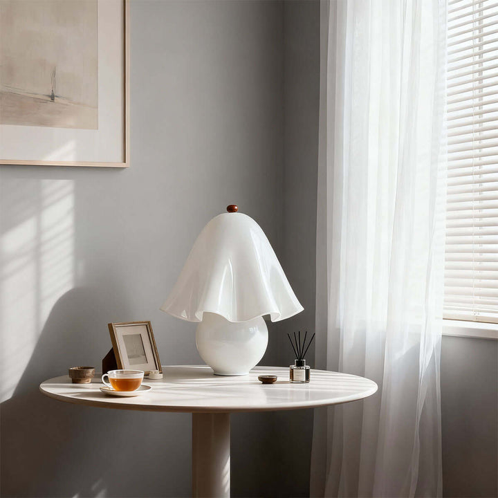 Smooth white flower table lamp on a round side table beside a sunlit window