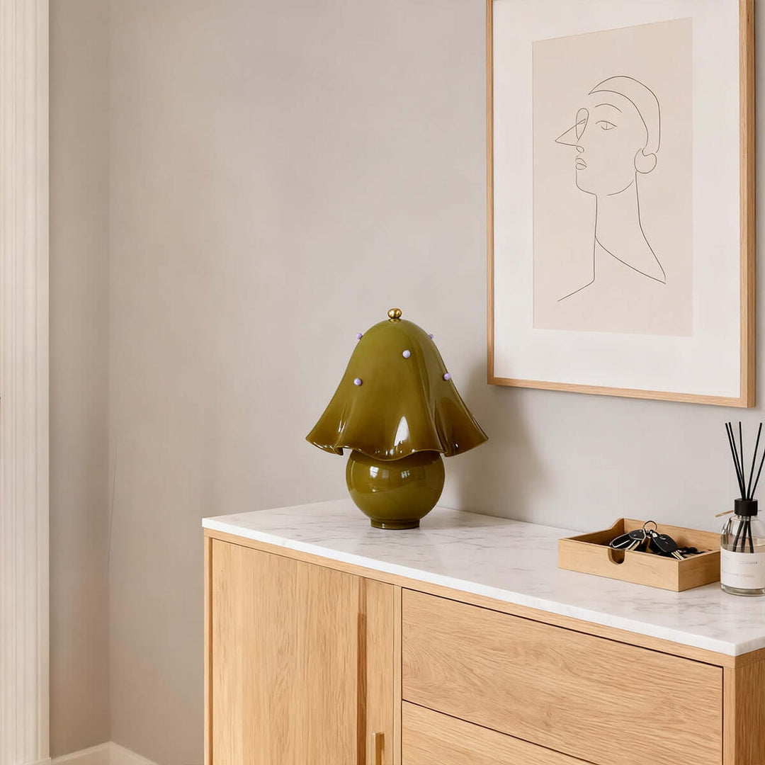 Spotted green glass table lamp on a light wood console beneath minimalist wall art