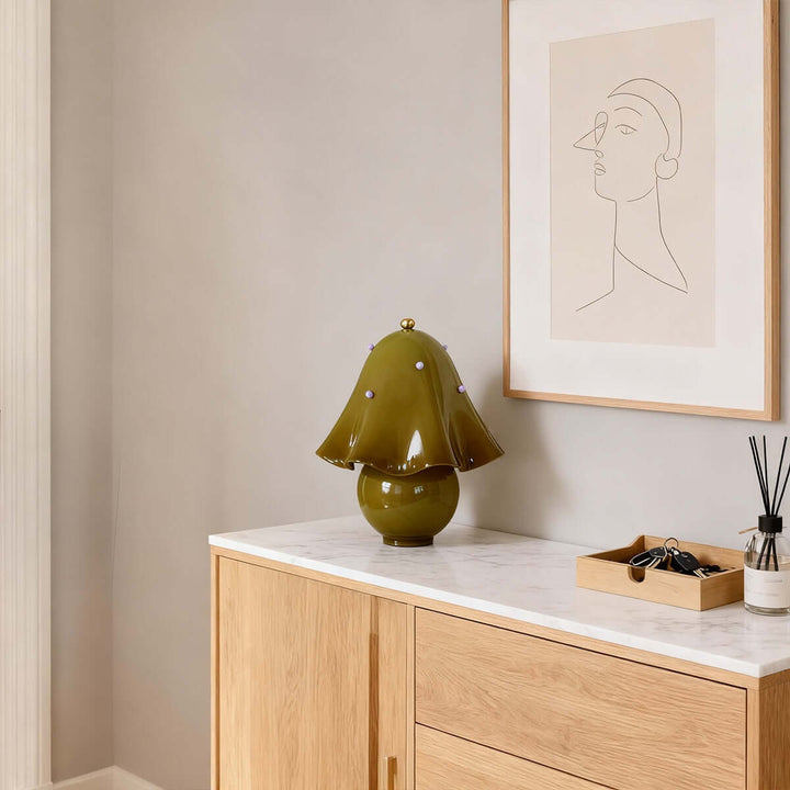 Spotted green glass table lamp on a light wood console beneath minimalist wall art