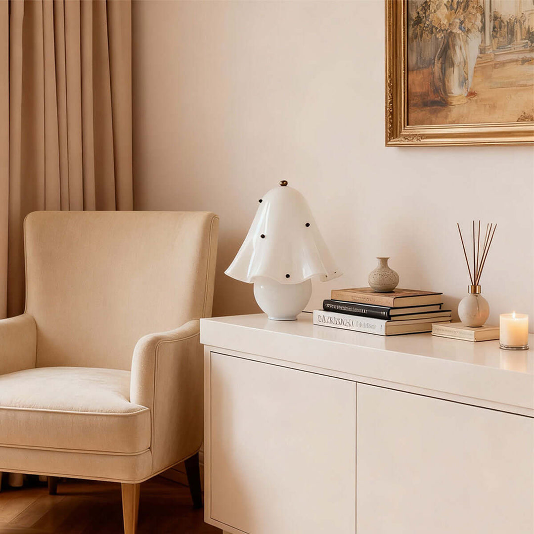 Spotted white glass table lamp on a modern console beside books and a lounge chair