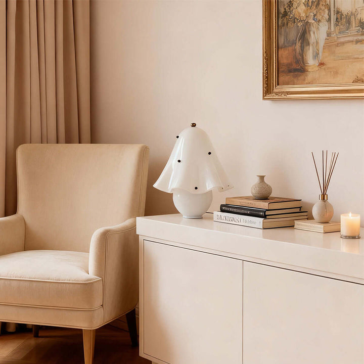 Spotted white glass table lamp on a modern console beside books and a lounge chair