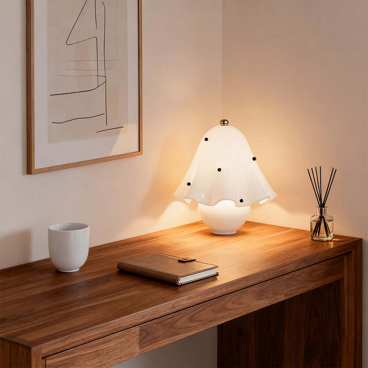 Spotted white glass table lamp glowing on a wood desk with books and a reed diffuser