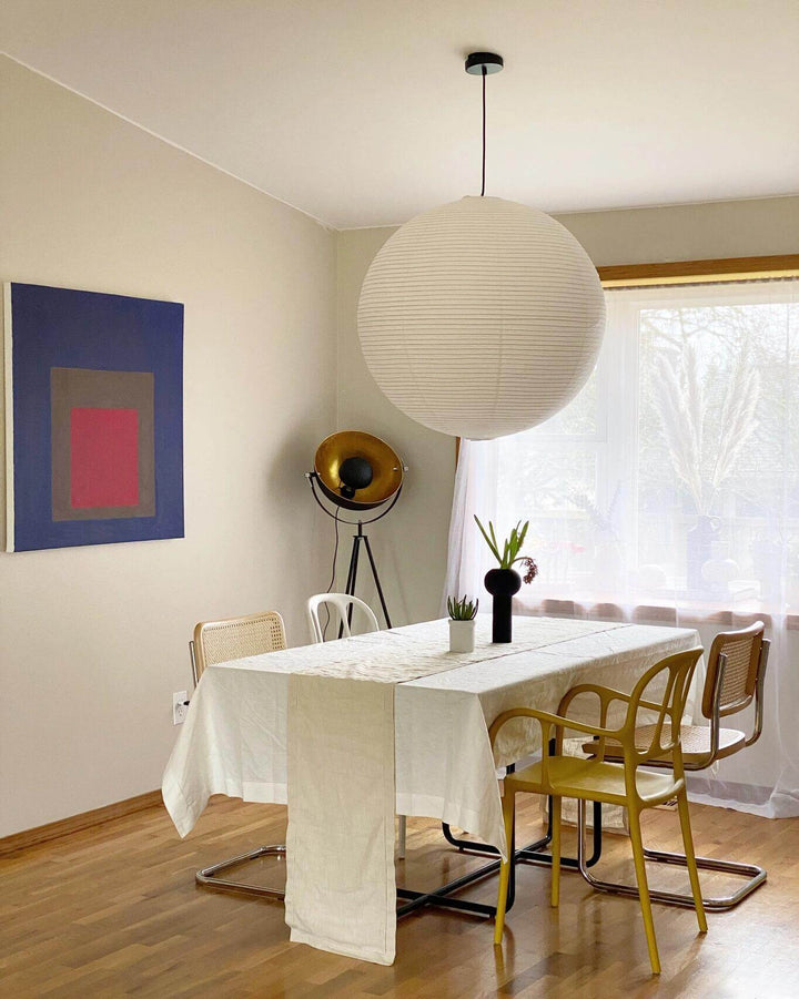 Oversized white paper pendant light above a dining table near a large window