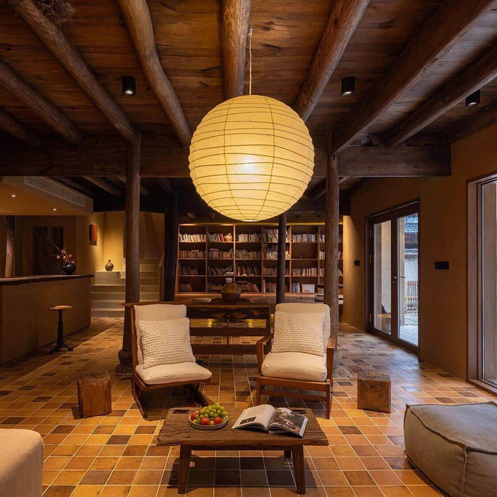 Large paper lantern pendant light glowing in a rustic living room with wood beams.