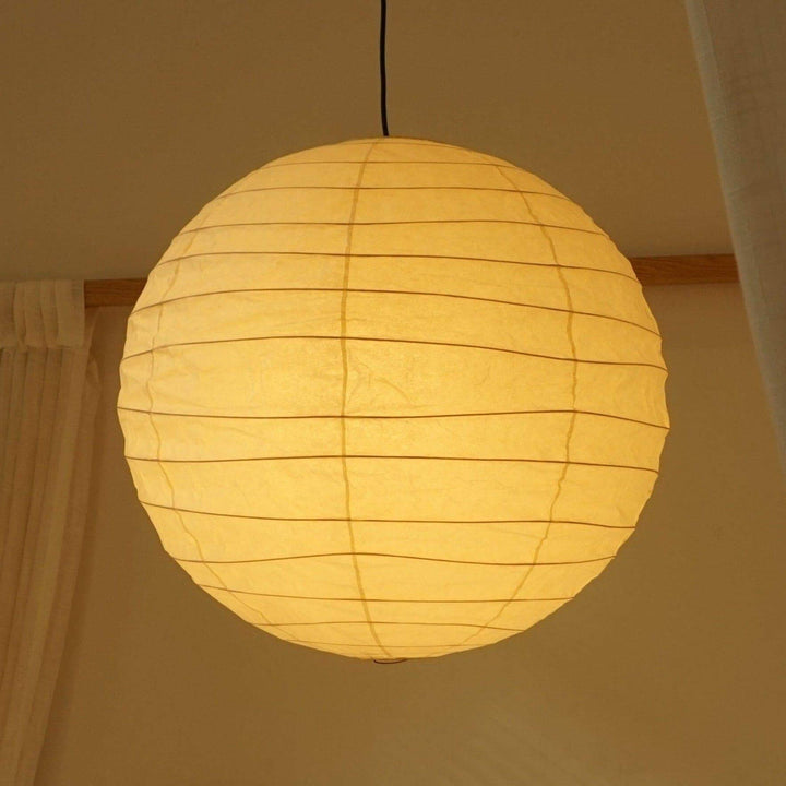 Close-up of a glowing paper lantern pendant light with black cord against a warm wall.