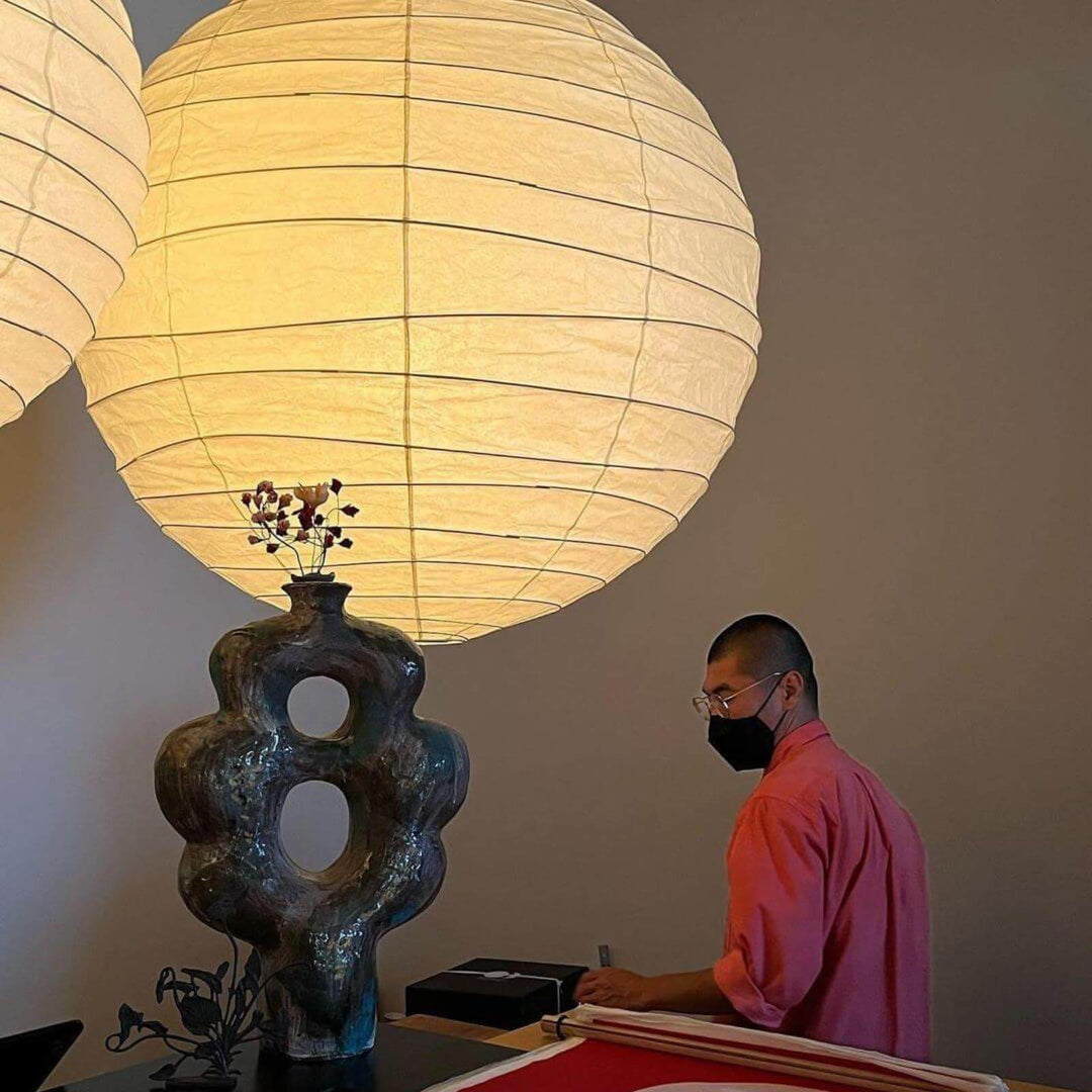 Oversized glowing paper lantern pendant light above a desk with a ceramic vase.