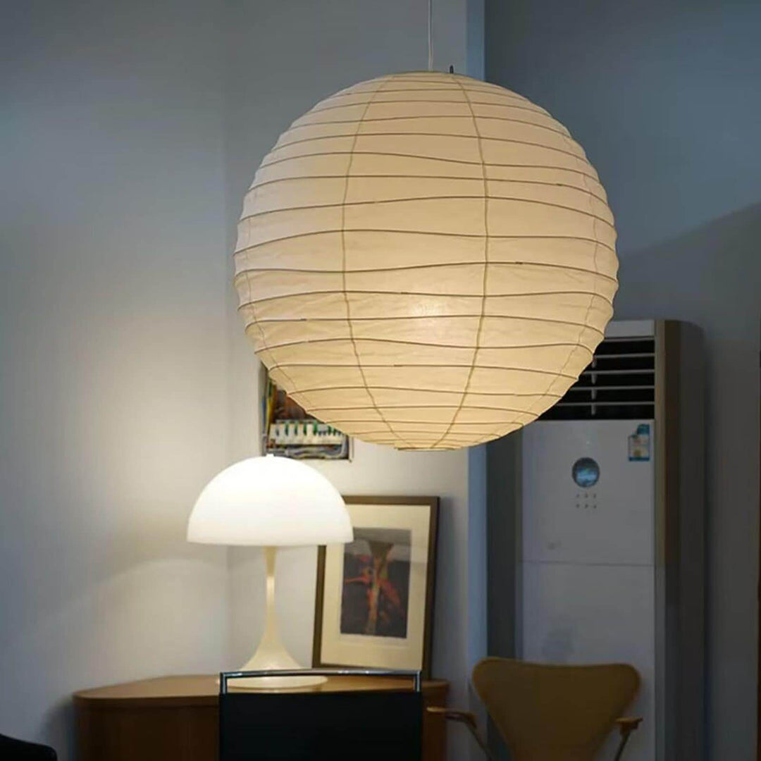 Paper lantern pendant light over a home corner with a table lamp and framed art.