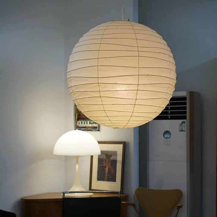 Paper lantern pendant light over a home corner with a table lamp and framed art.