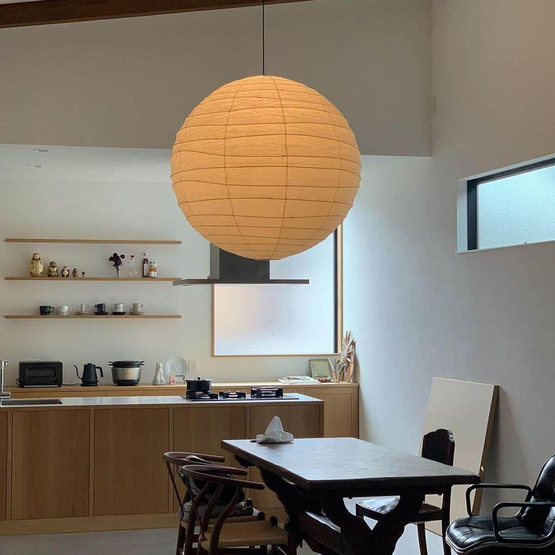 Round paper lantern pendant light over a kitchen dining area with shelves and wood cabinets.