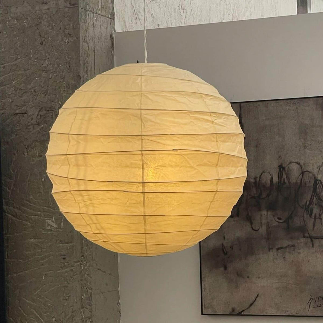 Close-up paper lantern pendant light glowing against textured concrete and abstract art.