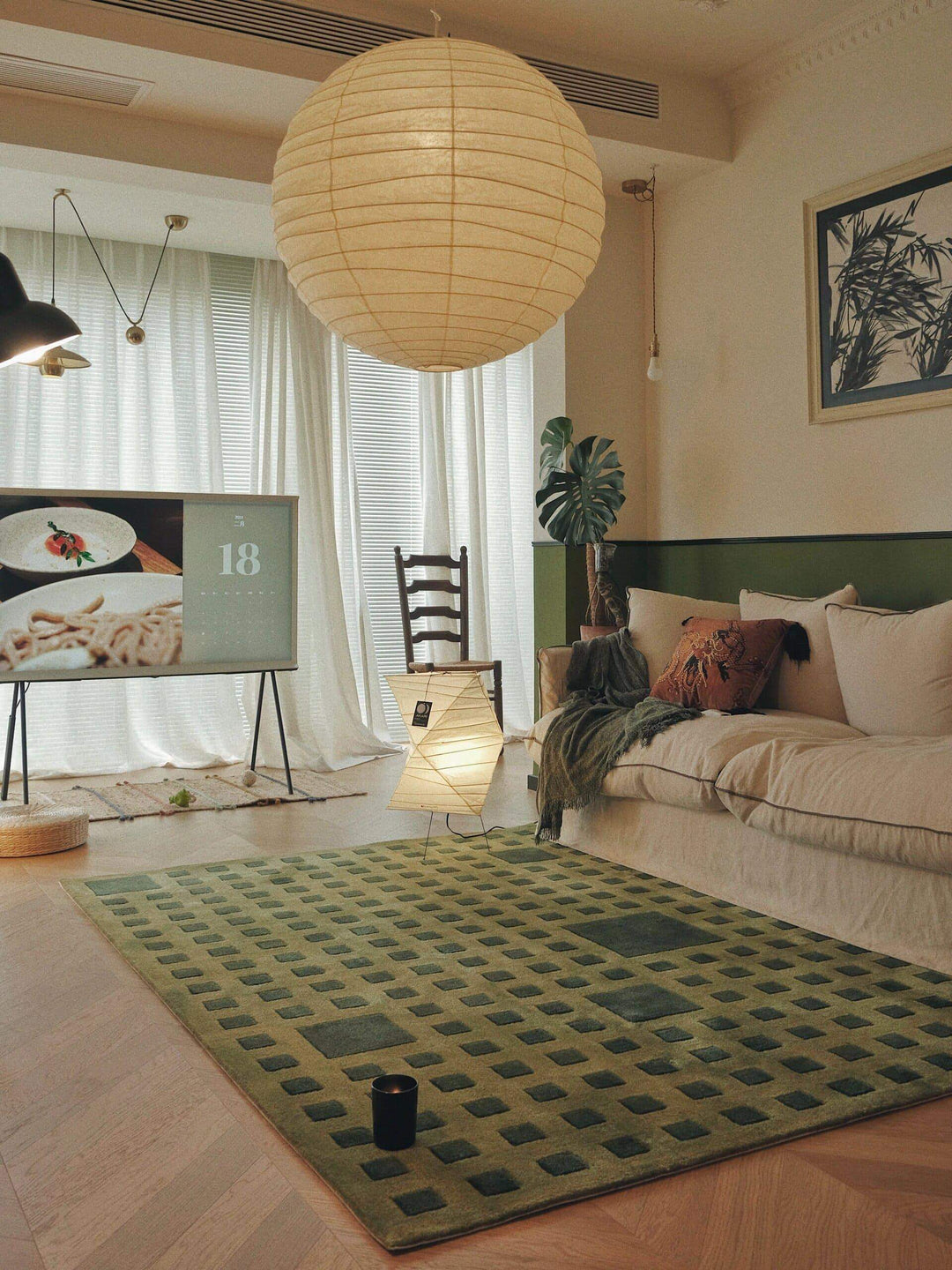 Large paper lantern pendant light in a living room with sofa, TV, green rug, and floor lamp.