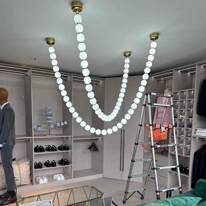 Glowing pearl necklace chandelier installed in a closet room with gold canopies and white globes.