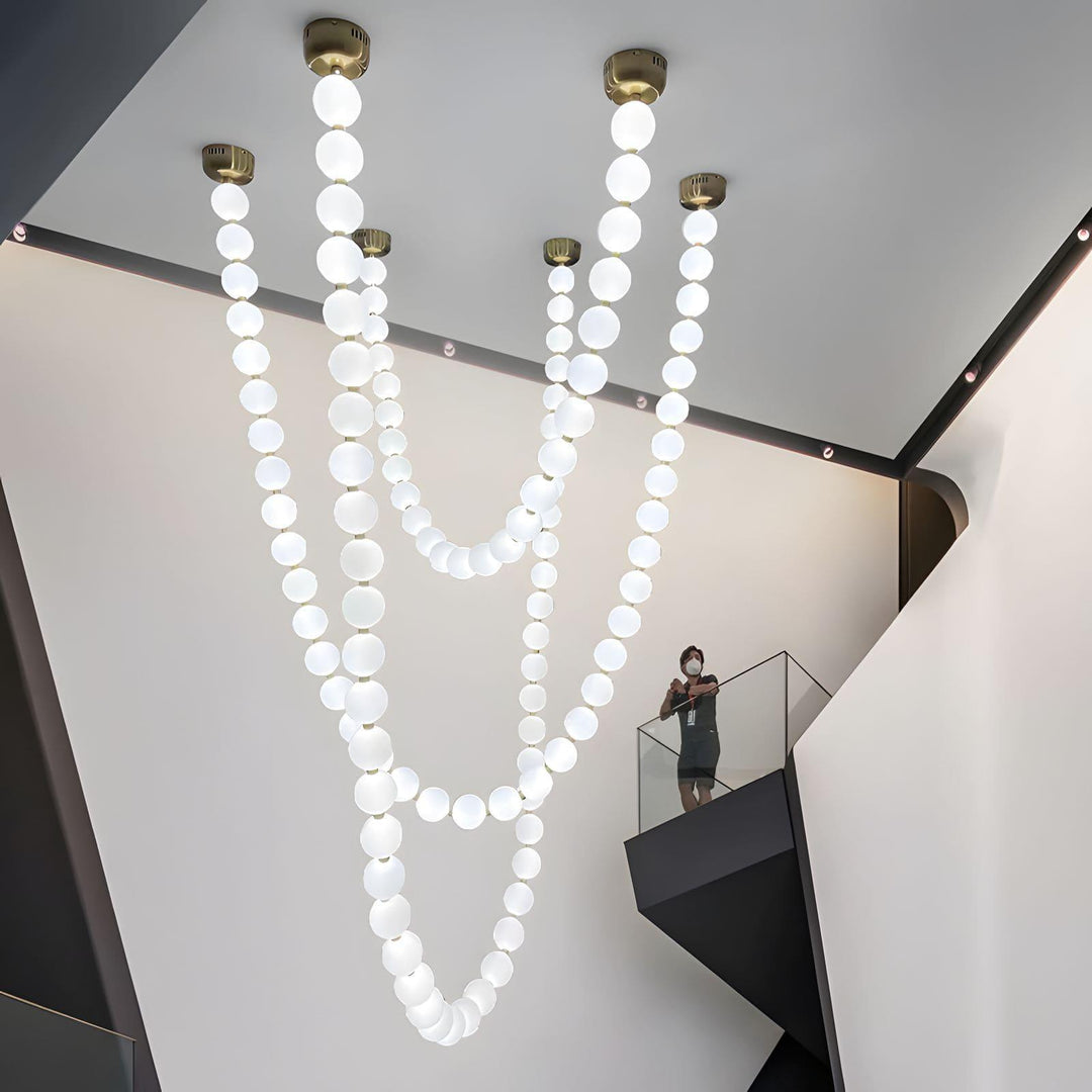 Large pearl necklace chandelier with multiple glowing strands in a tall atrium space.