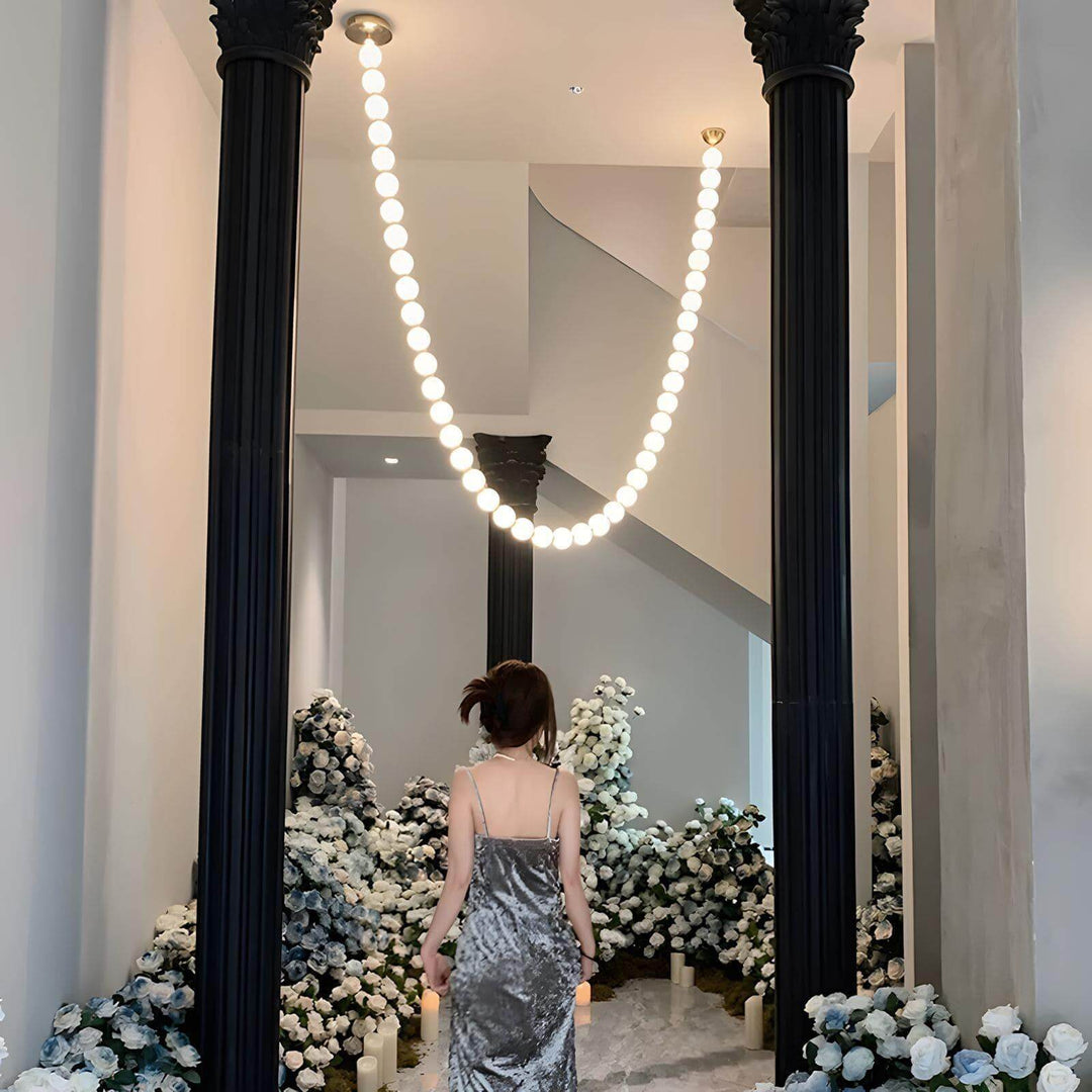 Pearl necklace chandelier glowing above a floral hallway with tall black columns.