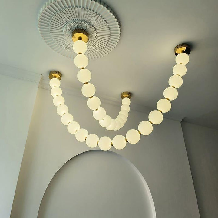 Warm pearl necklace chandelier with white globes and brass accents under a decorative ceiling medallion.