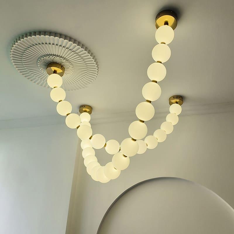 Close ceiling view of a pearl necklace chandelier with glowing globes and brass connectors.
