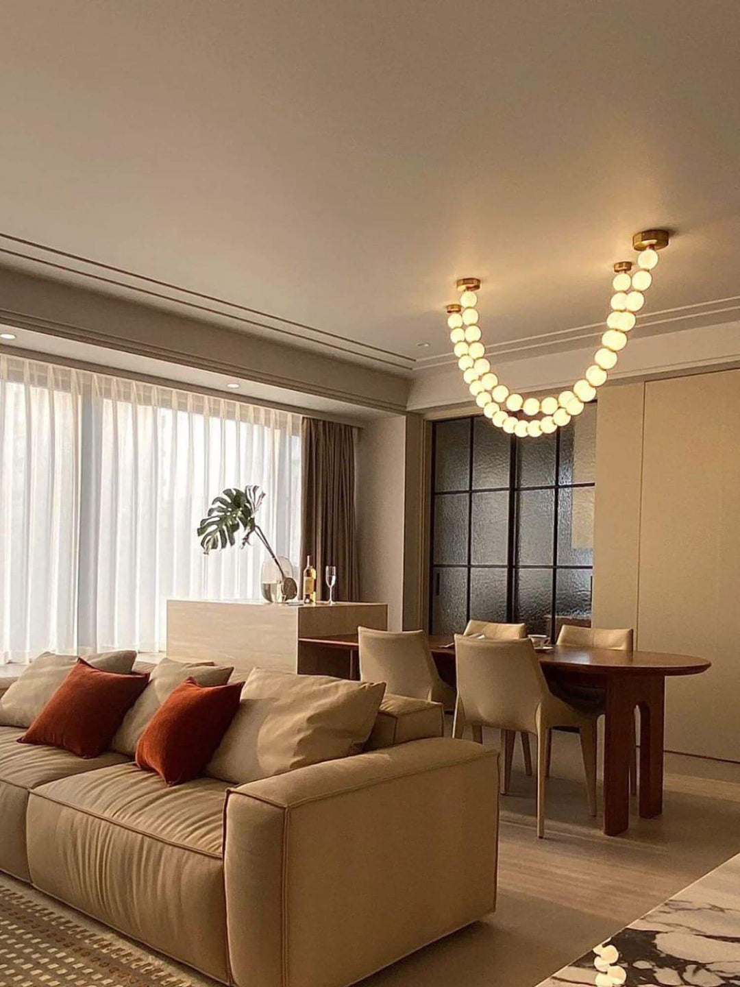 Pearl necklace chandelier glowing above a dining and living room with warm ambient light.