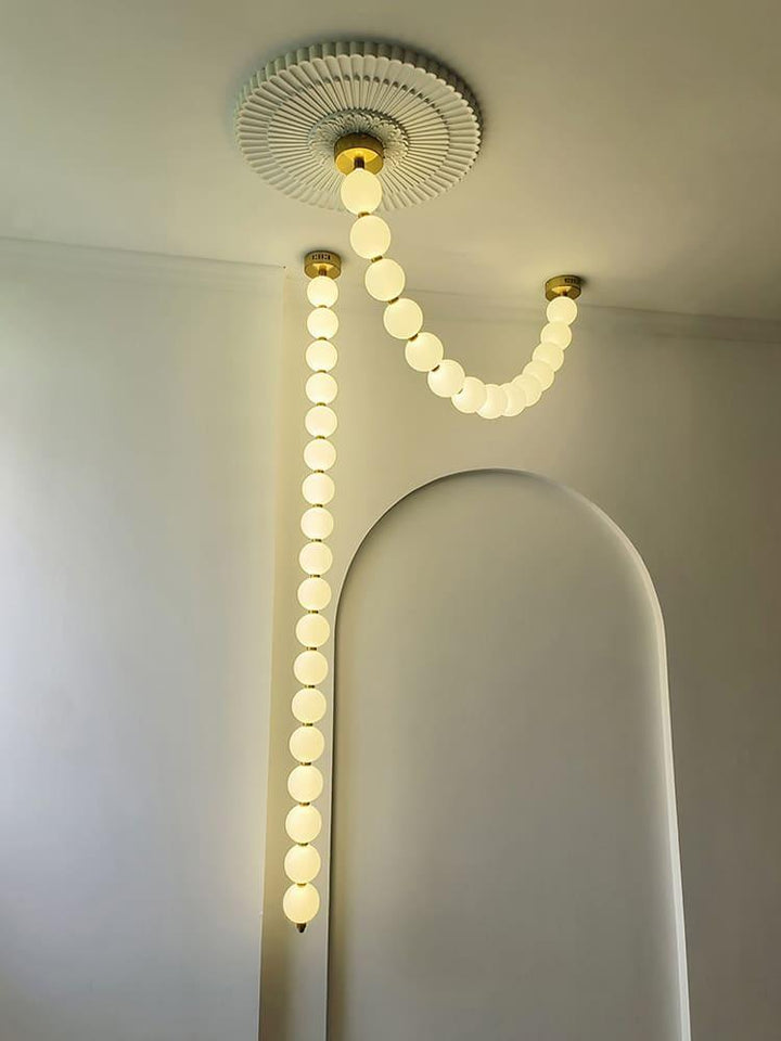 Pearl necklace chandelier installed near an arched wall with one vertical glowing globe strand.