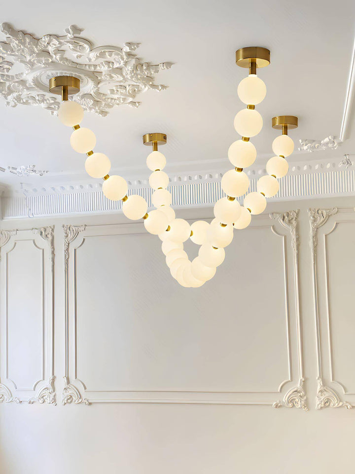 Multi-strand pearl necklace chandelier glowing on an ornate white ceiling with brass canopies.