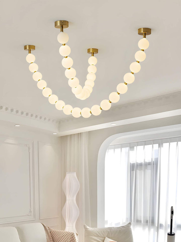 Modern pearl necklace chandelier glowing above a bright living room with white curtains.
