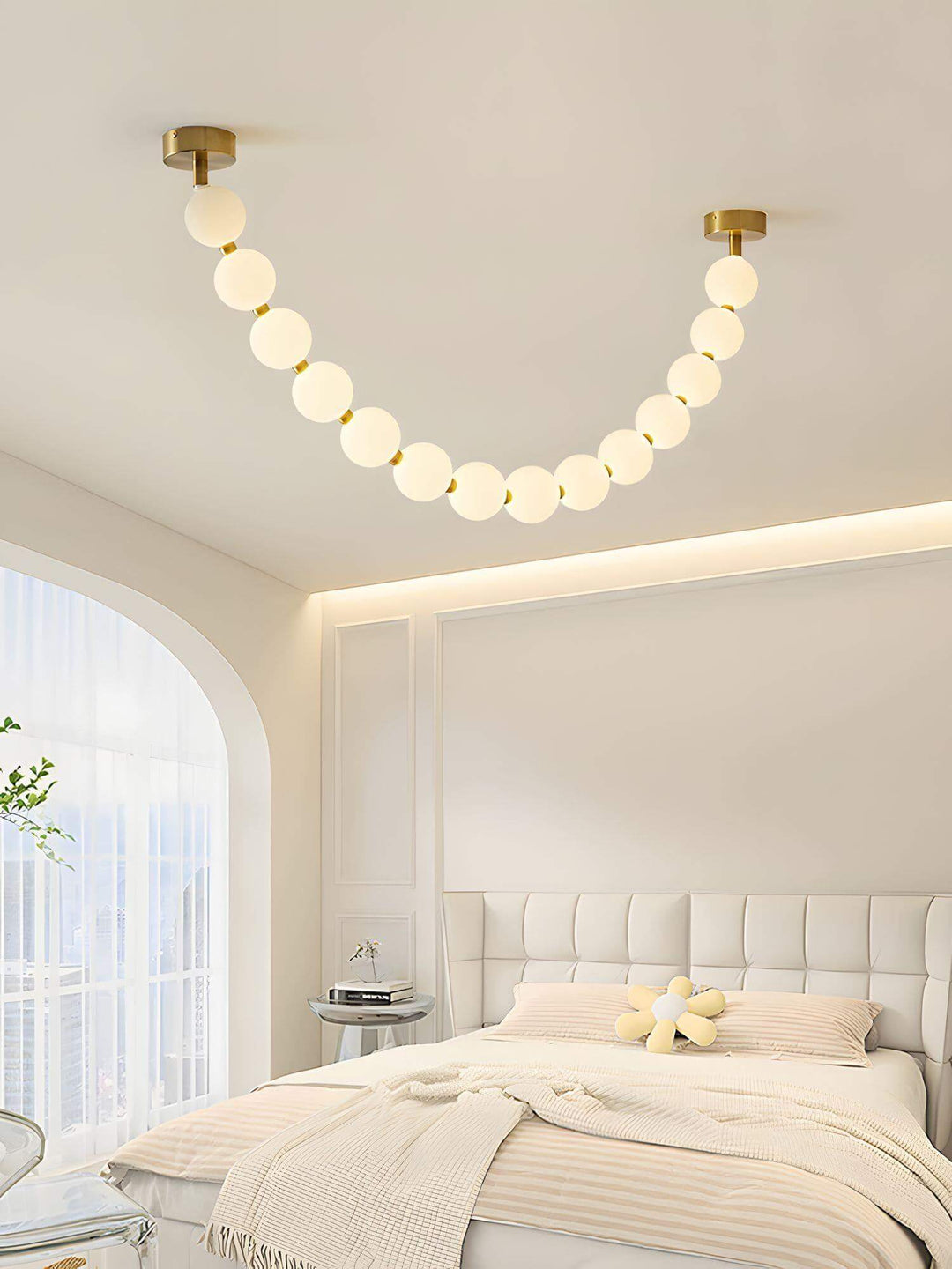 Pearl necklace chandelier above a soft bedroom with arched window and upholstered headboard.