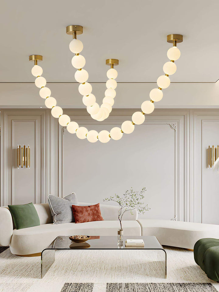 Large pearl necklace chandelier above a curved sofa and glass coffee table in a modern living room.