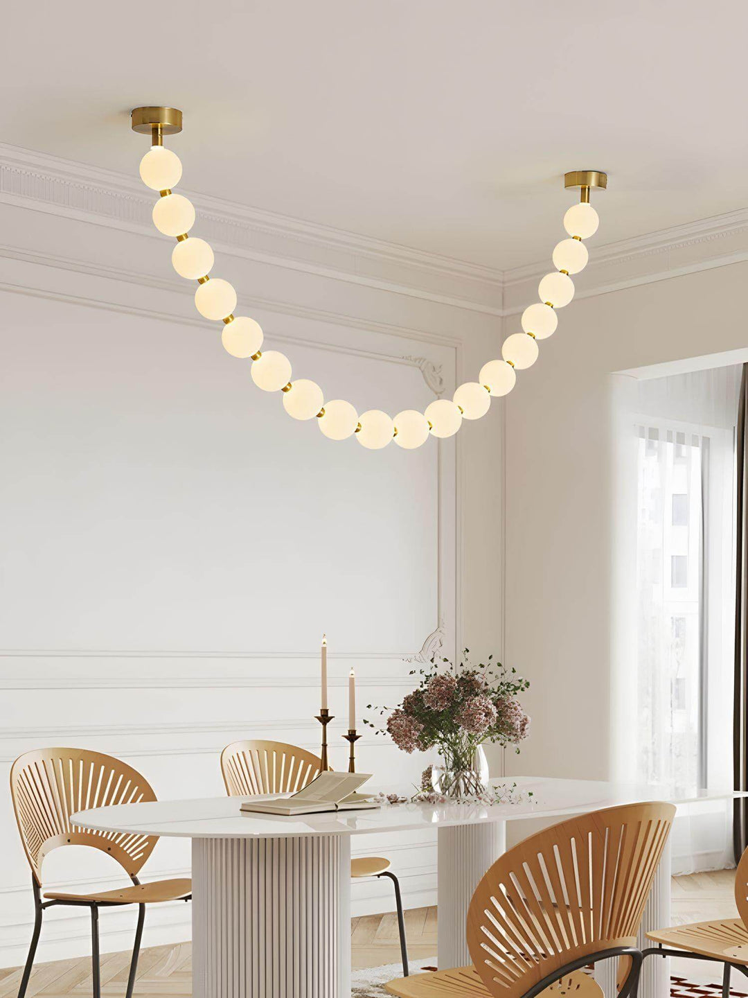 Pearl necklace chandelier above a white dining table with wood chairs and soft daylight.