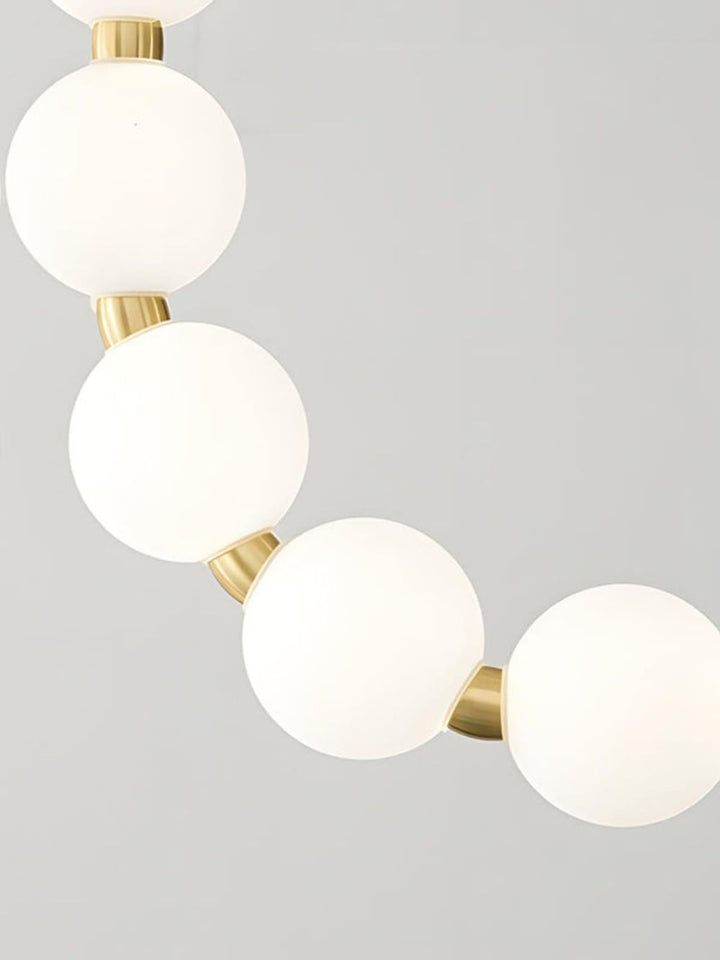 Close-up of white glowing globes and brushed gold connectors on a pearl necklace chandelier.