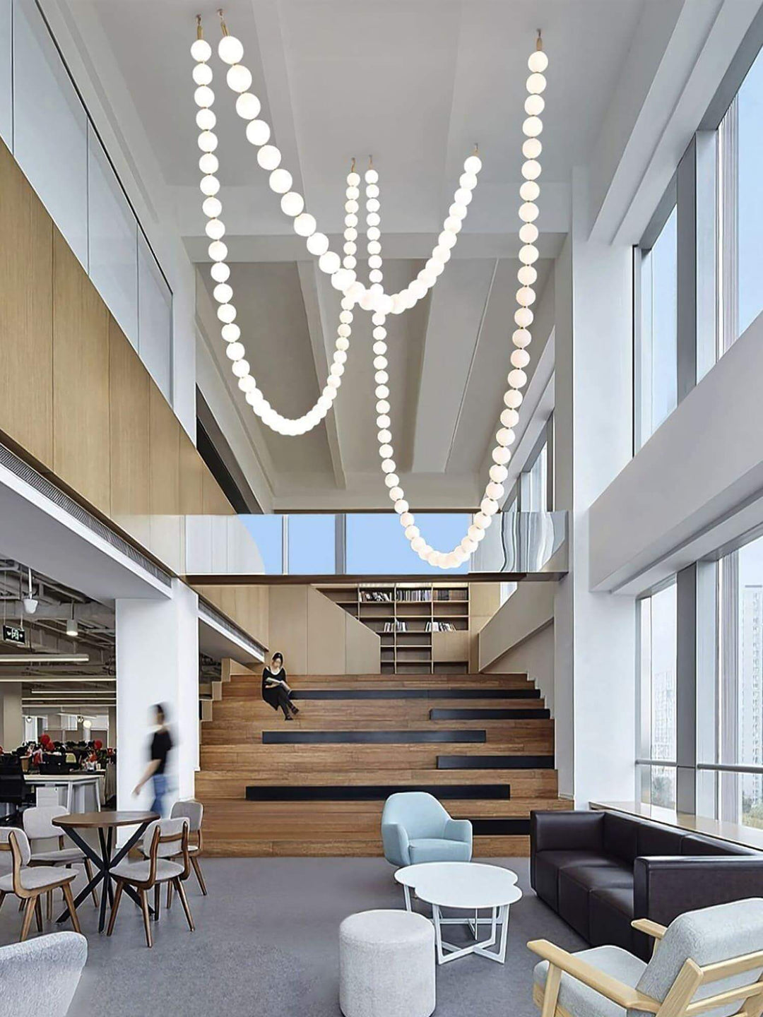 Oversized pearl necklace chandelier with long glowing strands in an open lounge atrium.