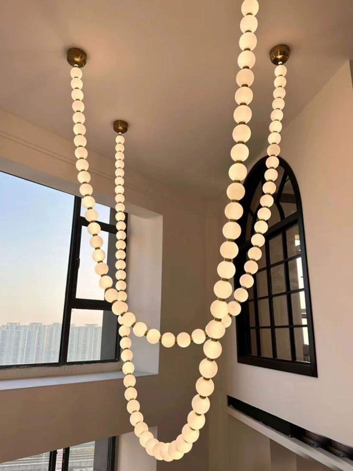 Large glowing pearl necklace chandelier in a tall corner space with black frame windows.