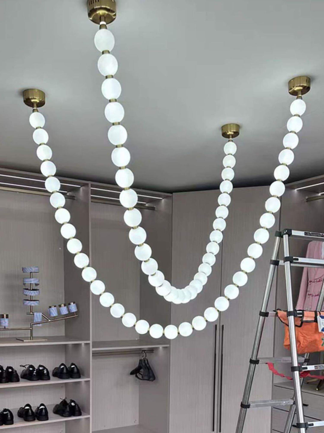 Cropped closet view of a glowing pearl necklace chandelier with multiple white globe strands.