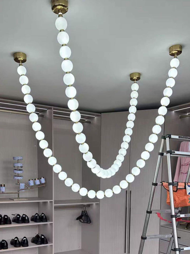 Cropped closet view of a glowing pearl necklace chandelier with multiple white globe strands.