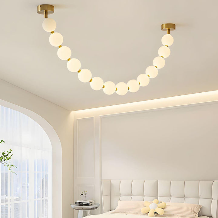 Close bedroom view of a pearl necklace chandelier above a bed and arched window.