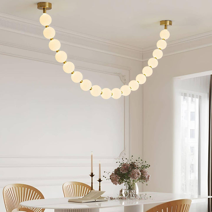 Close dining room view of a pearl necklace chandelier above a white table and wood chairs.