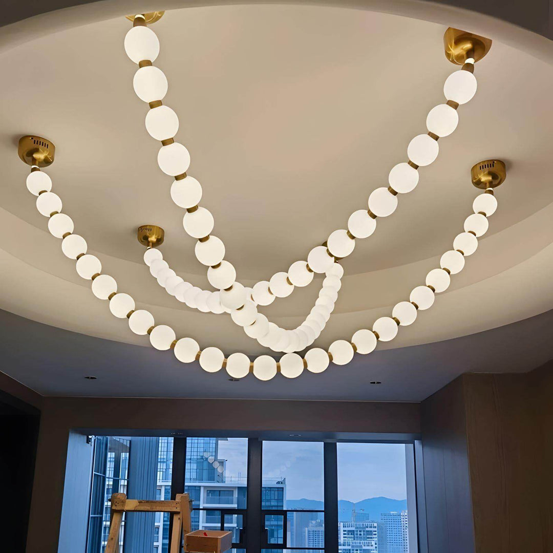 Large pearl necklace chandelier installed under a recessed ceiling with multiple glowing loops.