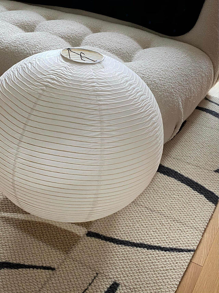 Round rice paper lantern shade resting on a rug with its top support frame visible