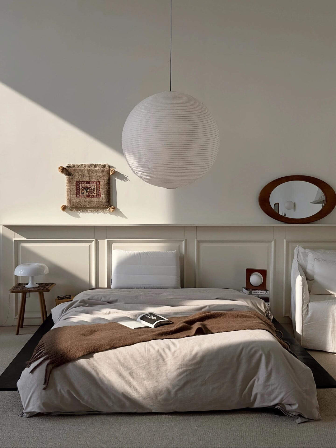 Round white paper lantern pendant above a sunlit neutral bedroom
