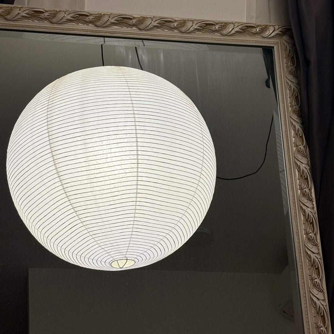 Upper portion of a round rice paper pendant light reflected in an ornate mirror