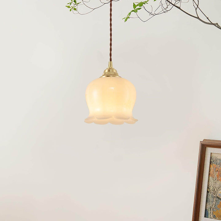 Small flower pendant light with an illuminated beige resin shade and antique brass hardware