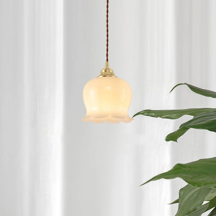 Small hanging light with a warm flower-shaped shade beside green plants and white curtains