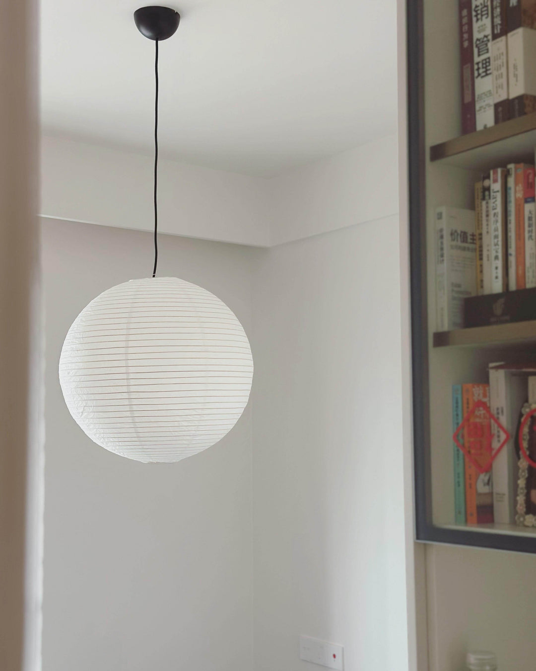 Small unlit rice paper pendant with a black wire beside a study bookcase
