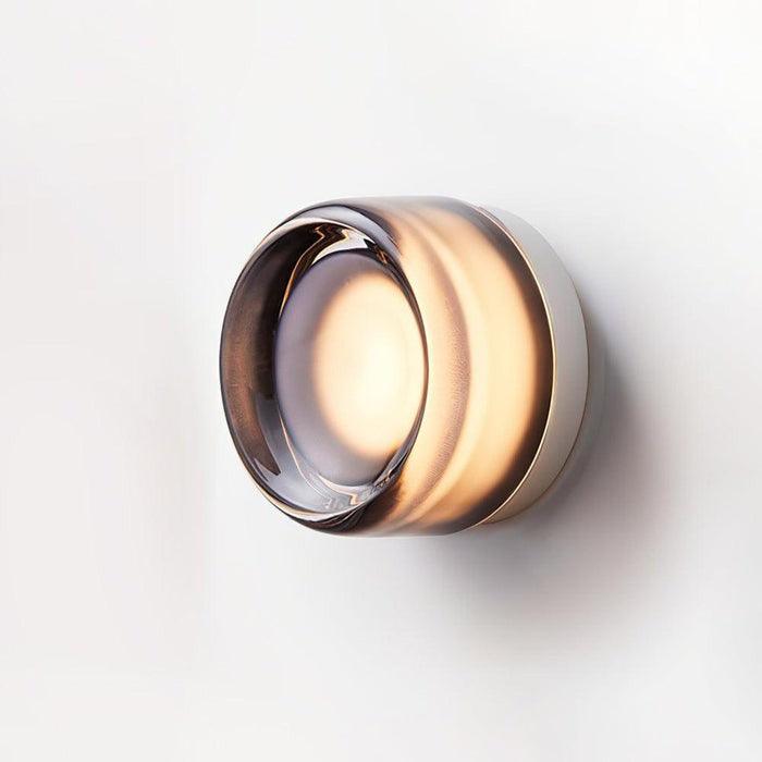 Smoke gray glass wall sconce lit on a white background with a warm glow.