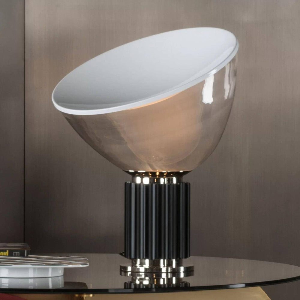 Close view of the Taccia glass table lamp with a black fluted base on a reflective glass tabletop