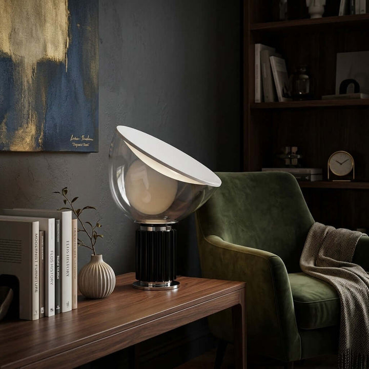 Black Taccia table lamp on a wood console in a dark home library with a green velvet chair
