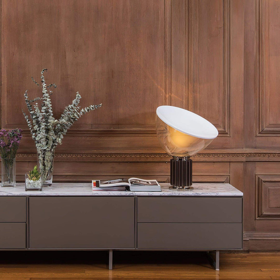 Illuminated coffee Taccia table lamp on a marble console against a rich wood-paneled wall