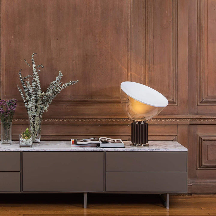 Illuminated coffee Taccia table lamp on a marble console against a rich wood-paneled wall