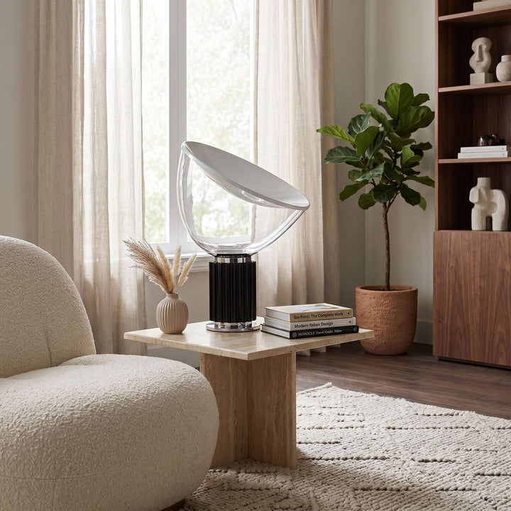 Black Taccia table lamp on a wood side table beside a curved cream chair in a bright living room
