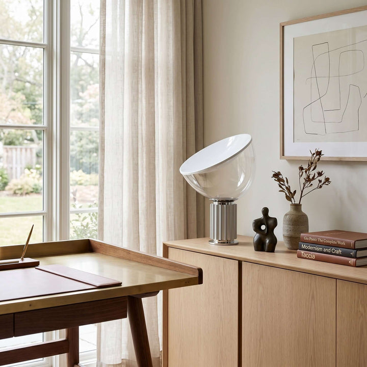 Silver Taccia table lamp on a light wood sideboard beside a home office desk and tall window