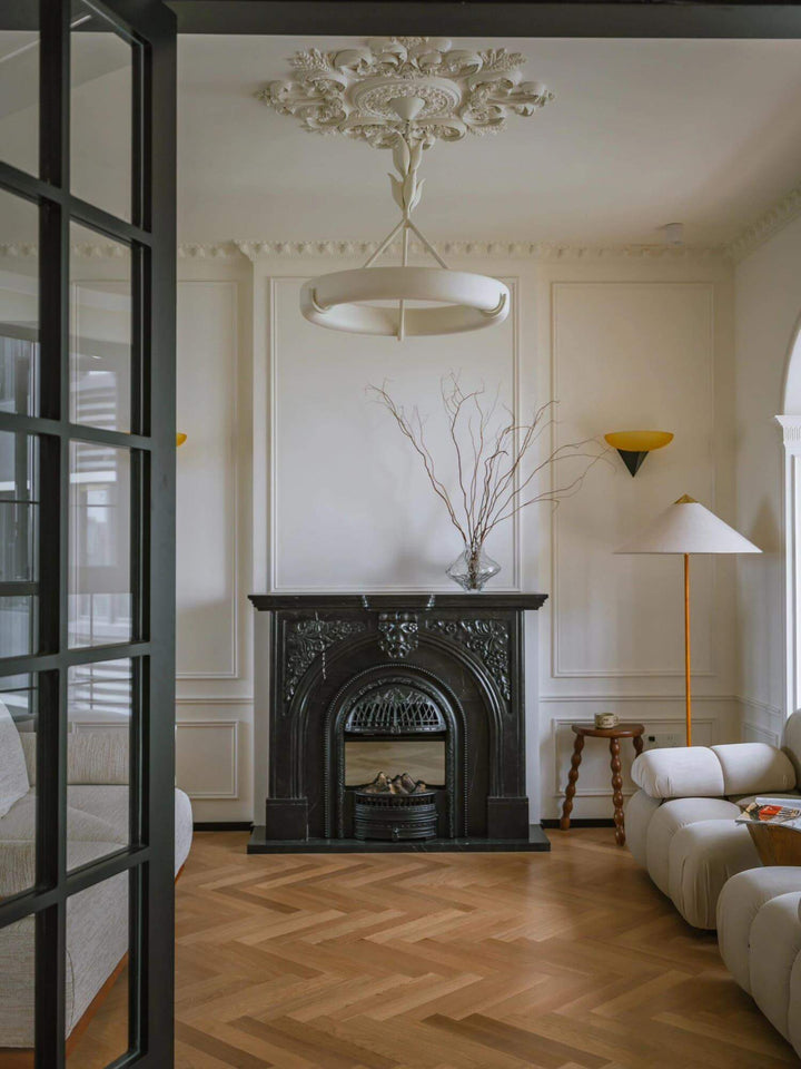Tinsley white ring chandelier above a classic living room with a black fireplace and herringbone wood floor.
